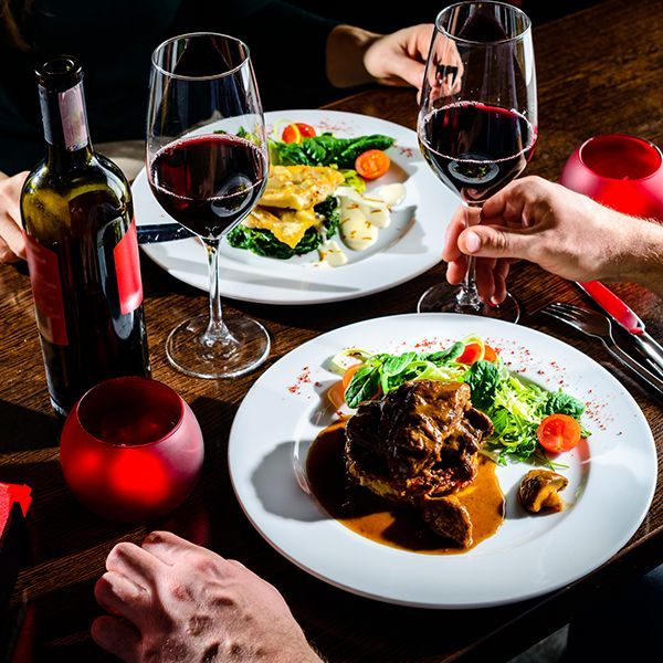 Two people are sitting at a table with plates of food and glasses of wine. Two people are sitting at a table with plates of food and glasses of wine.