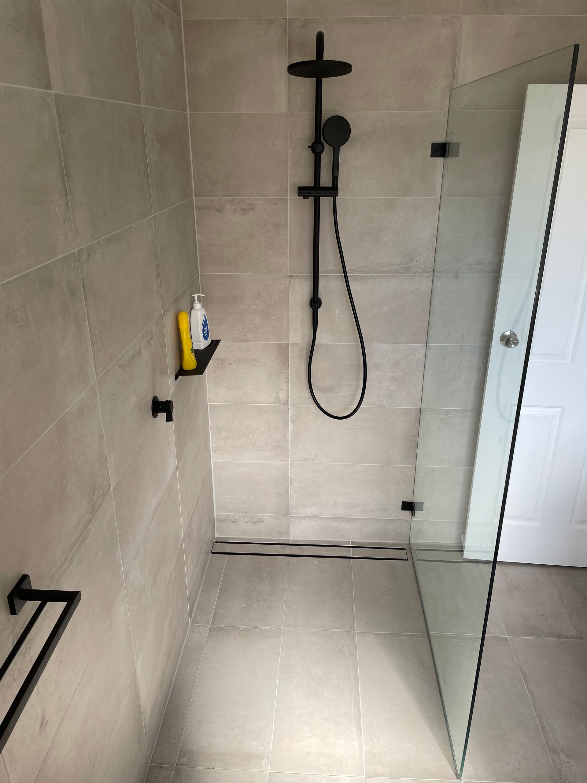 Modern tiled shower with black rainfall showerhead and glass door in a bathroom. Modern tiled shower with black rainfall showerhead and glass door in a bathroom.