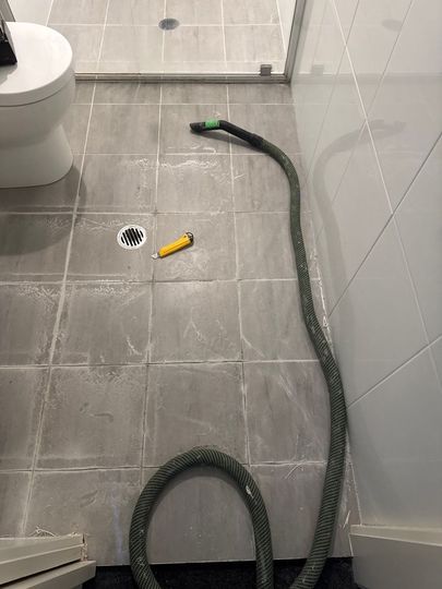 Bathroom floor with a long flexible hose coiled near a drain and a yellow-handled tool nearby
