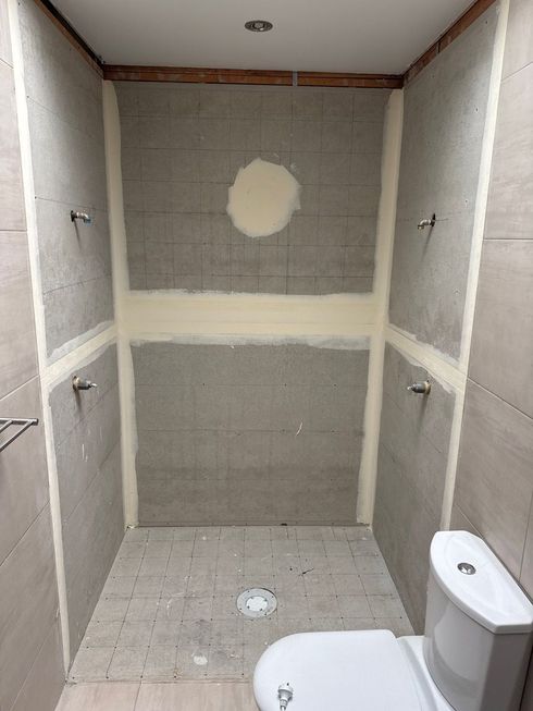 Empty tiled shower with gray walls, built-in shelves, and a toilet visible in the foreground.