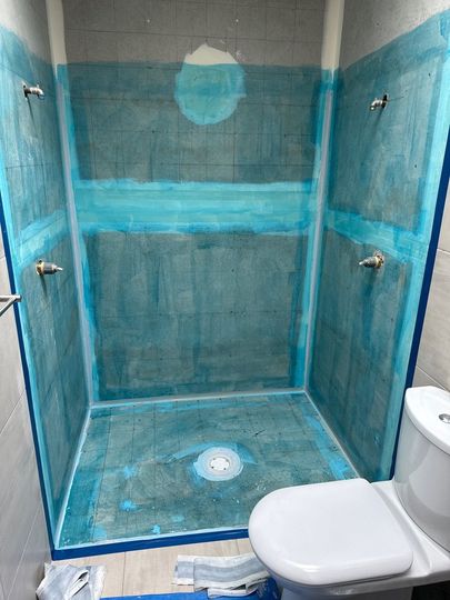 Small bathroom shower under renovation, blue waterproofing on walls and floor with a toilet beside it.