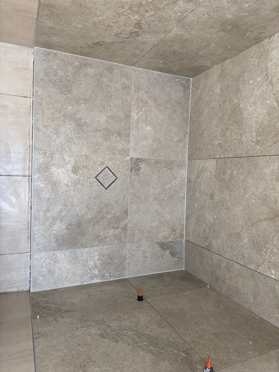 Empty gray tiled shower stall with a small square accent tile on the back wall.