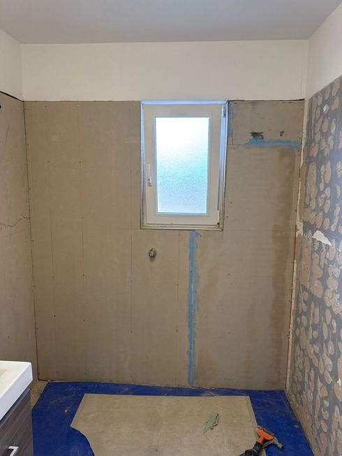 Small unfinished bathroom with a window, blue flooring, and partially stripped walls.