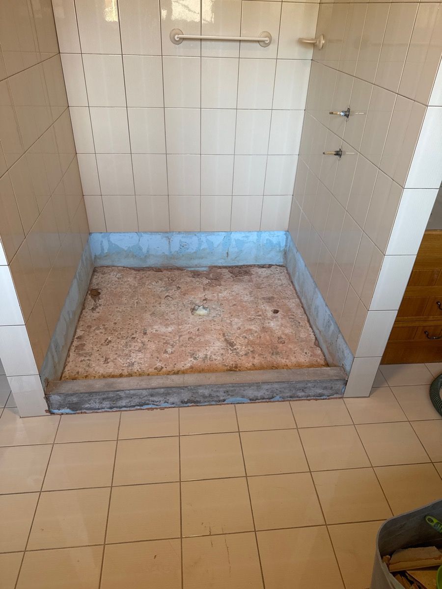 Empty tiled shower stall with a worn, stained floor and a grab bar on the back wall.