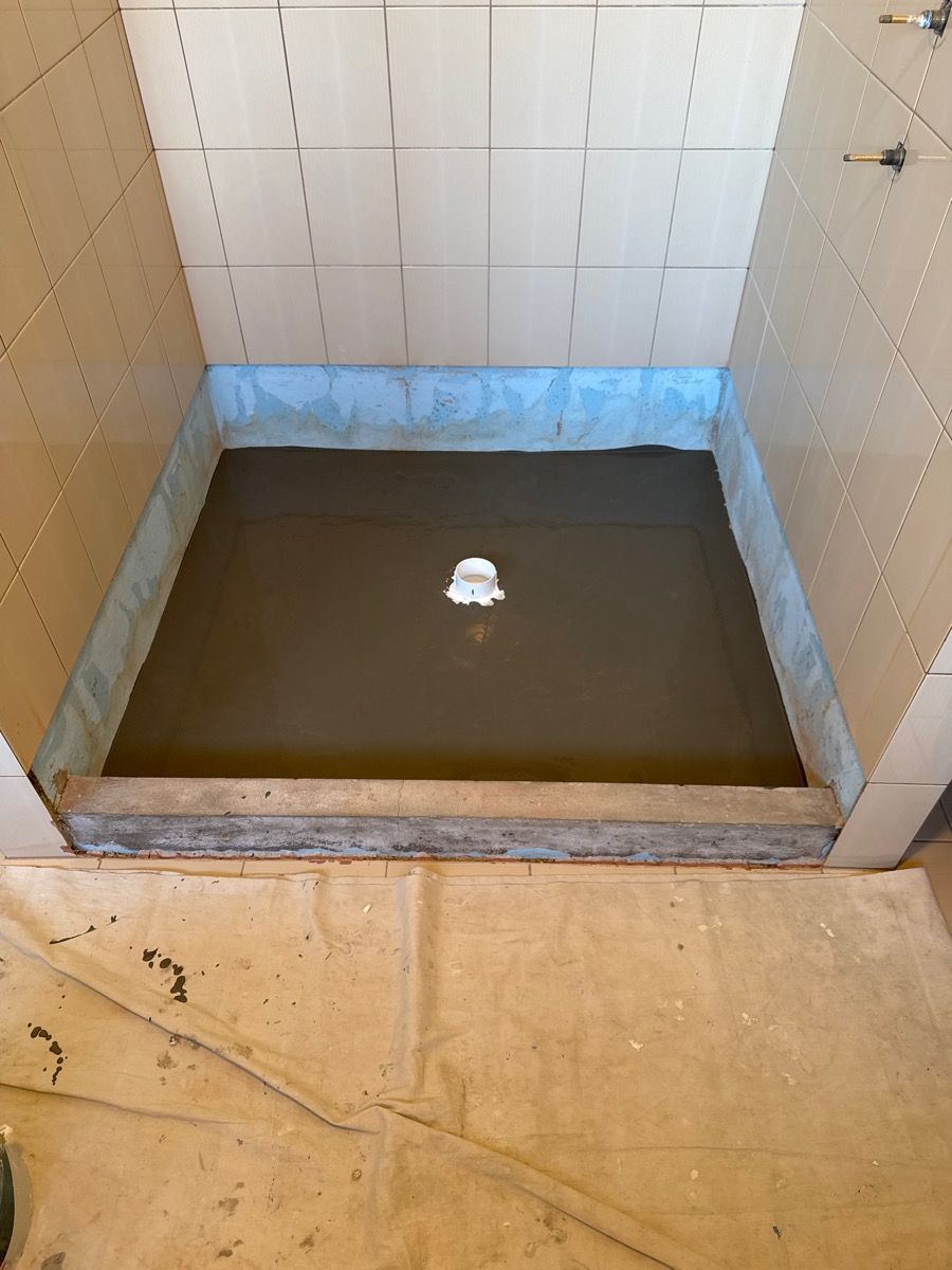 Bathroom shower stall with a shallow pool of muddy water and a small white object in the center.