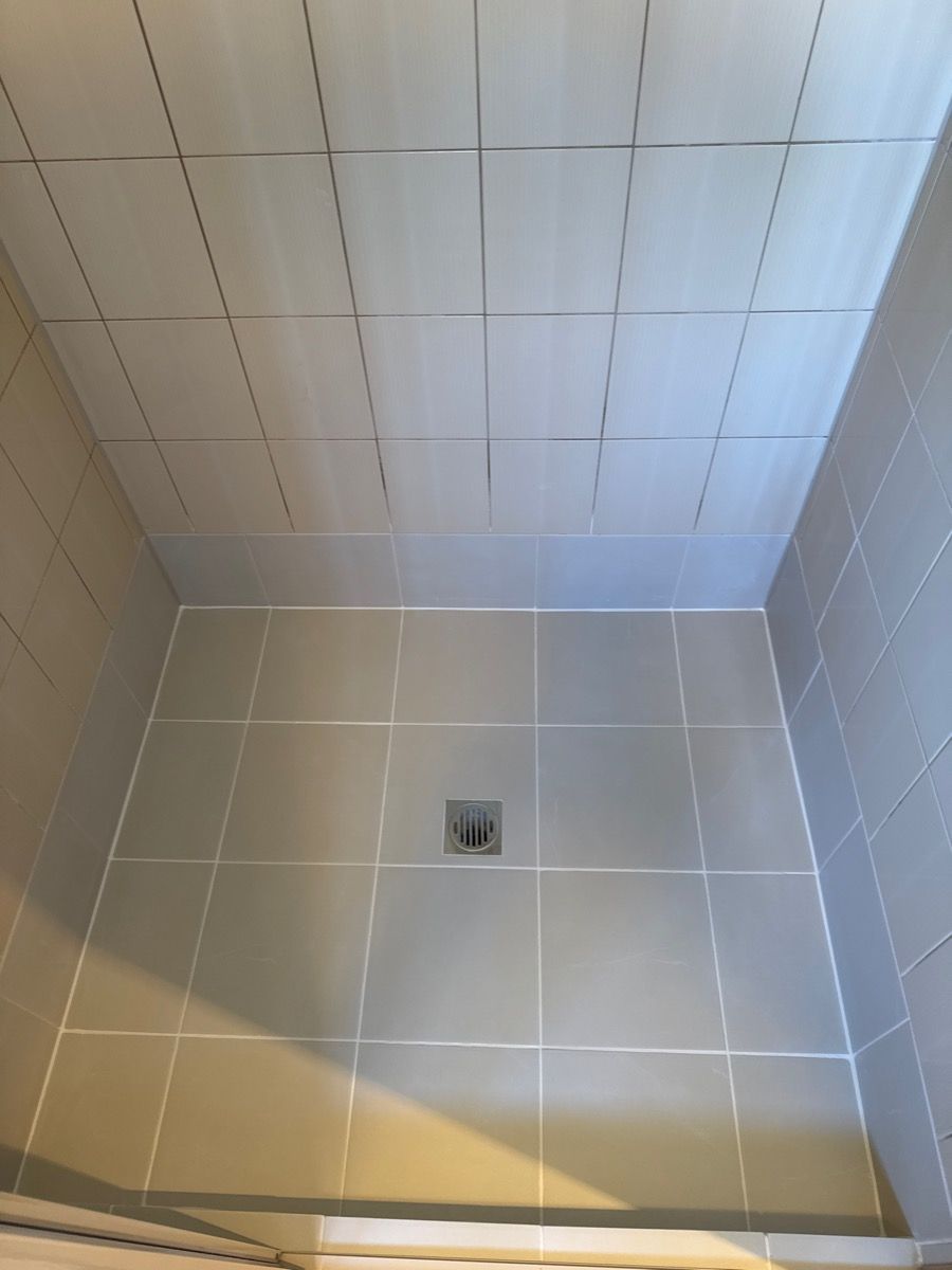 Empty tiled shower stall with a small floor drain