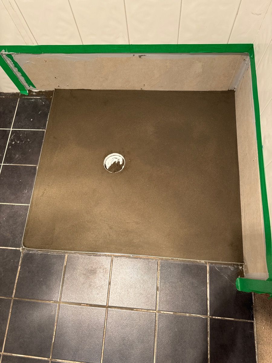 Bathroom floor with a square brown shower base and a drain, bordered by black tile and green trim.