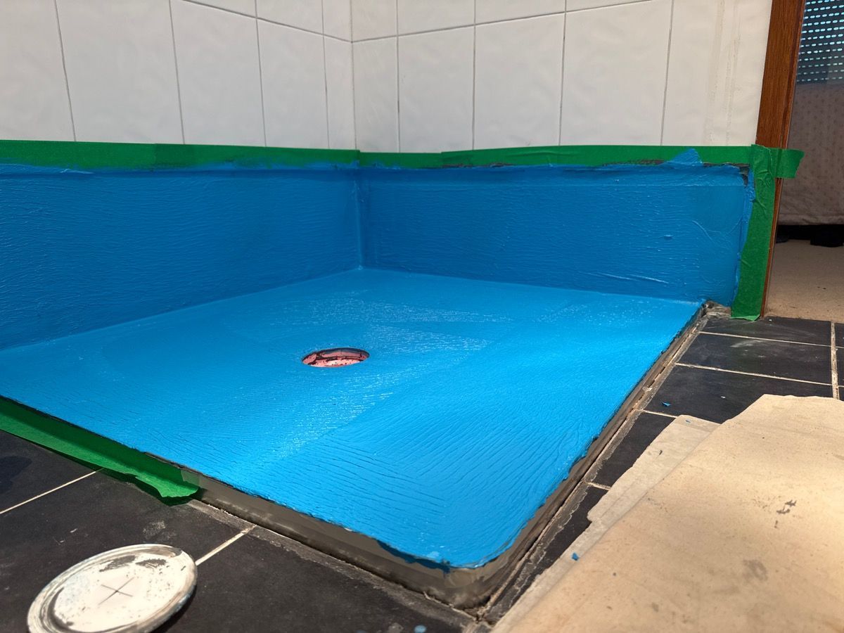 Empty blue indoor pool with green edging and tiled floor, with a drain cover near the center.