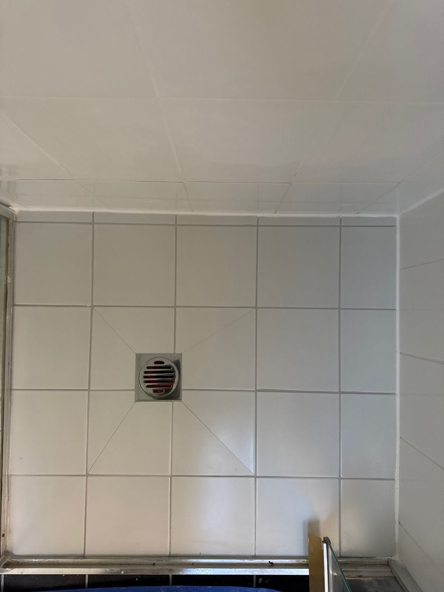 White tiled wall with a small square opening and a black metal bar at the bottom