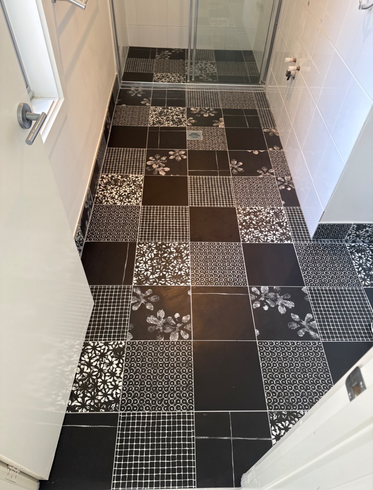 Black-and-white patterned tile floor in a narrow bathroom or hallway with a mirrored wall.