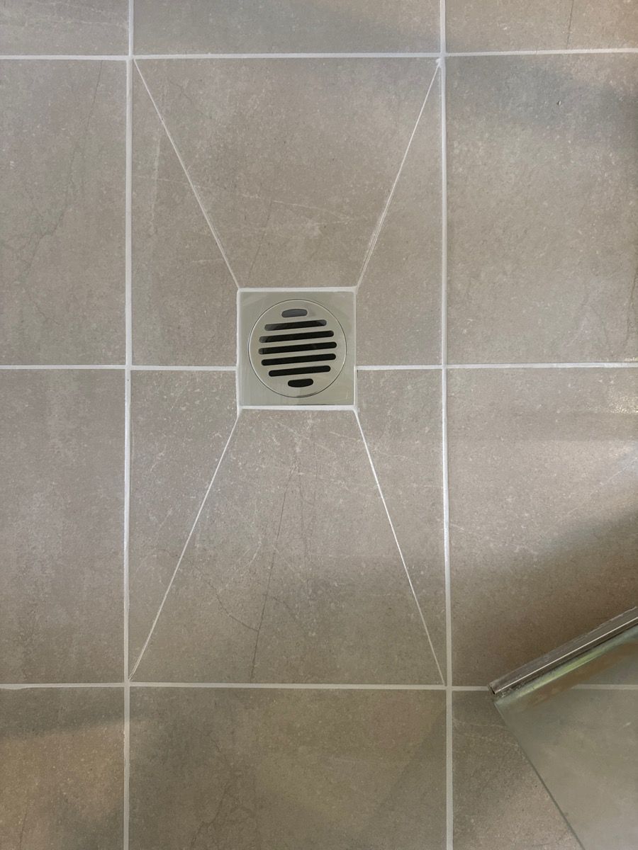 Close-up of a gray tiled shower floor with a square drain in the center. Close-up of a gray tiled shower floor with a square drain in the center.