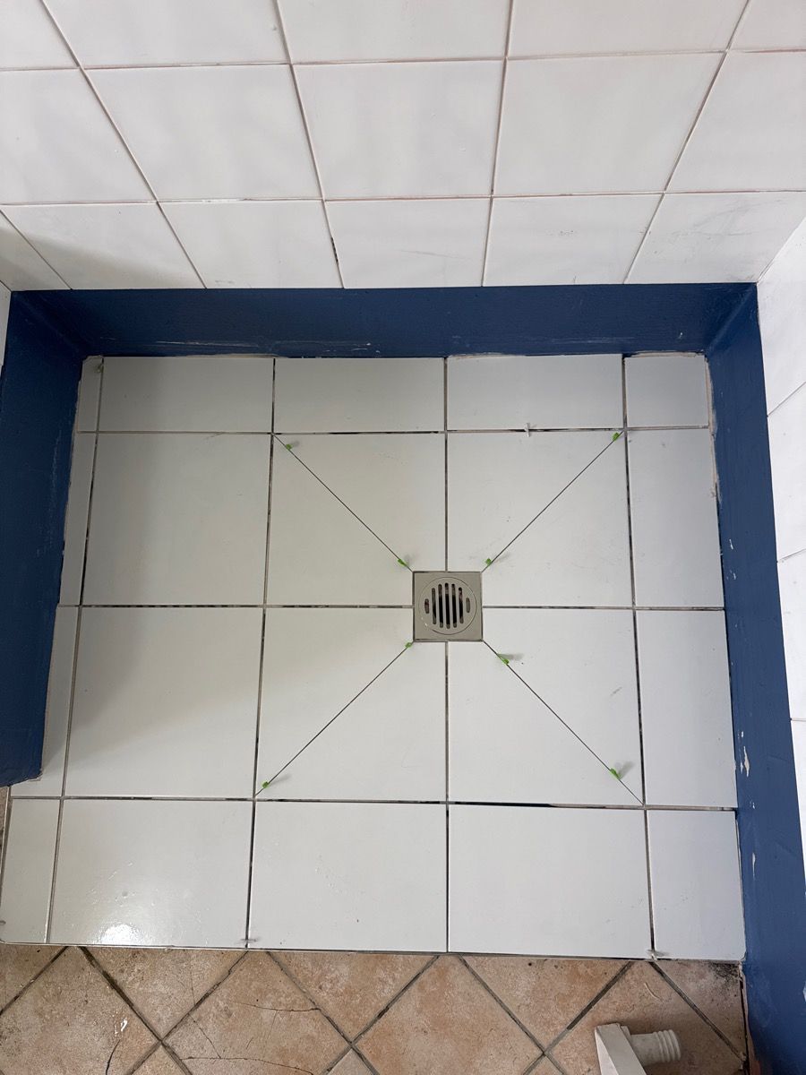 White tiled shower floor with a central drain and dark blue border trim