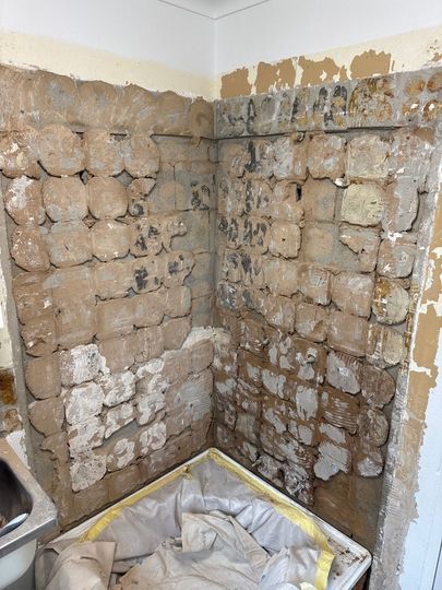 Corner of a room with stripped plaster walls, exposed stone or brick, and a covered floor area during renovation