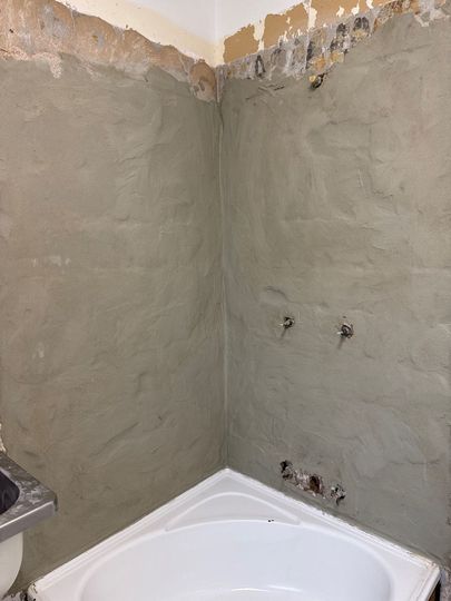 Unfinished bathroom with gray plastered walls and a white bathtub at the bottom.