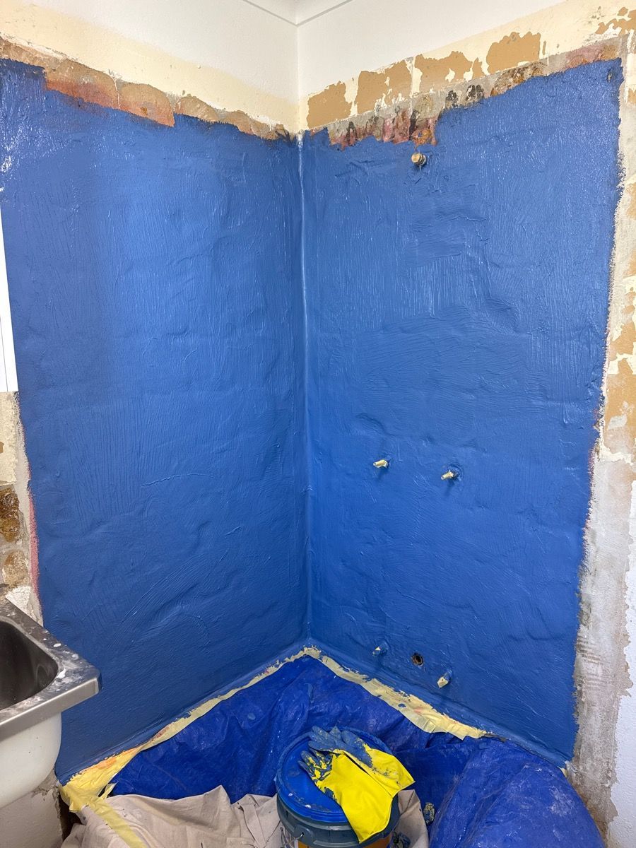 Blue-painted bathroom corner with exposed plaster near the ceiling and a covered shower or tub area below
