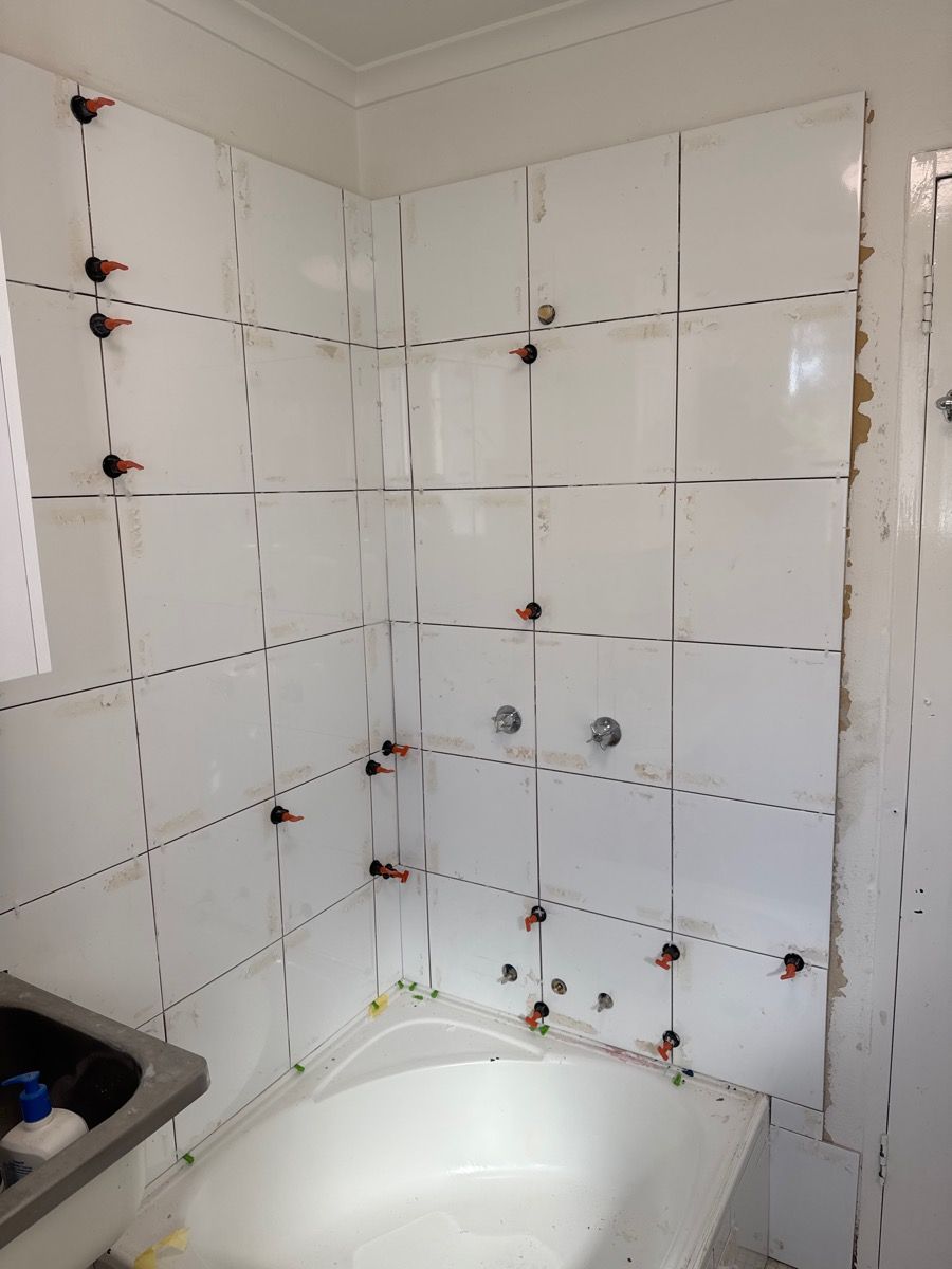 Partially tiled bathroom wall above a bathtub, with exposed patchwork and drill holes.