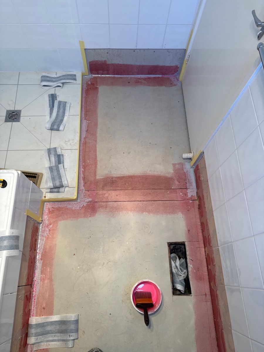Bathroom floor under construction with red waterproofing around a toilet drain and wall baseboards