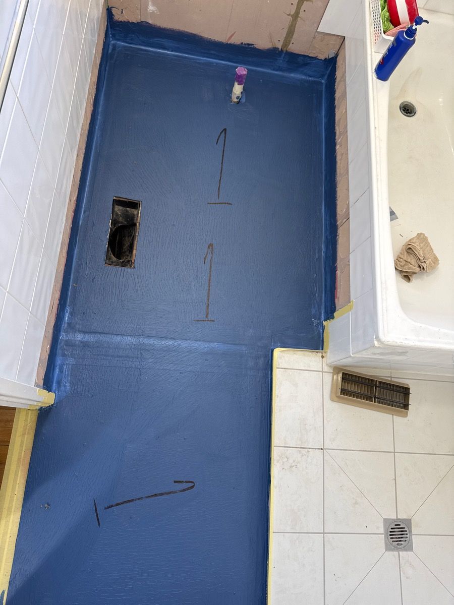 Blue floor in a small room with a drain, wall corner, and a few scattered items.