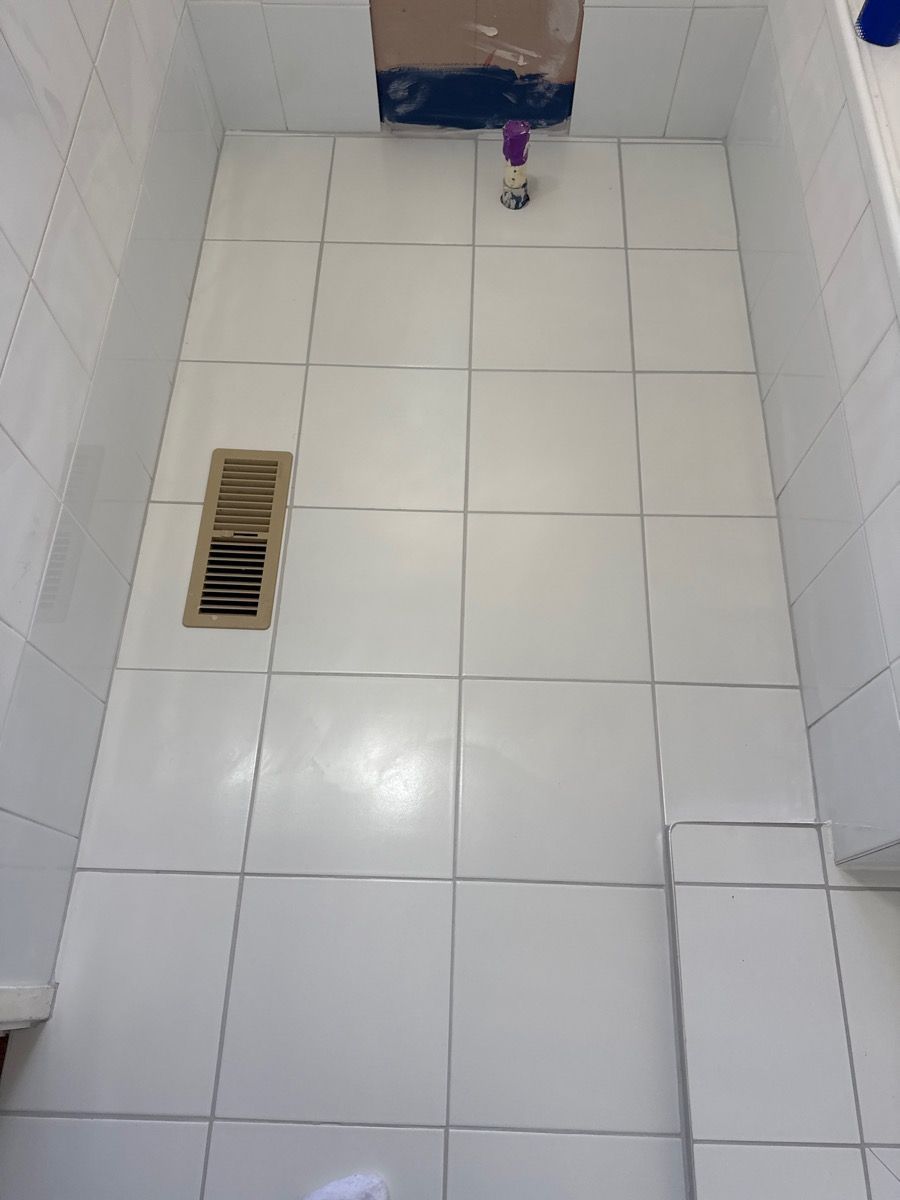 White tiled bathroom floor with a floor drain and a small purple object near the back wall. White tiled bathroom floor with a floor drain and a small purple object near the back wall.