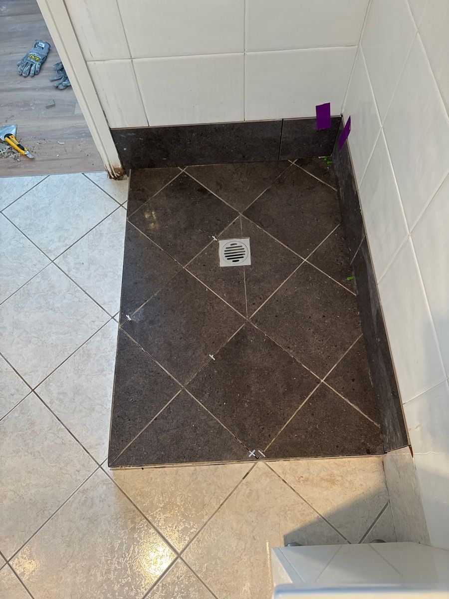 Small tiled bathroom corner with a dark shower floor and square drain grate. Small tiled bathroom corner with a dark shower floor and square drain grate.