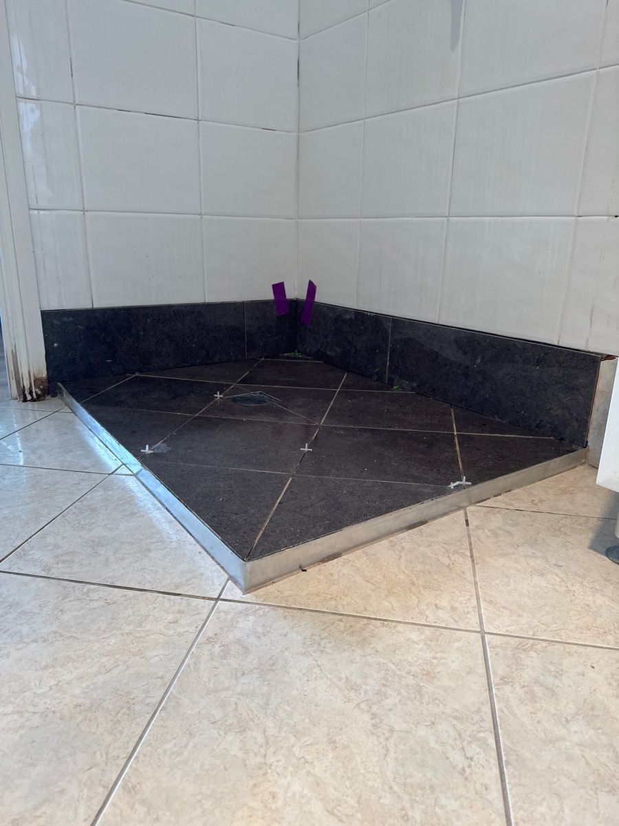 Tiled corner shower with a dark sloped floor and a small purple object at the back wall.