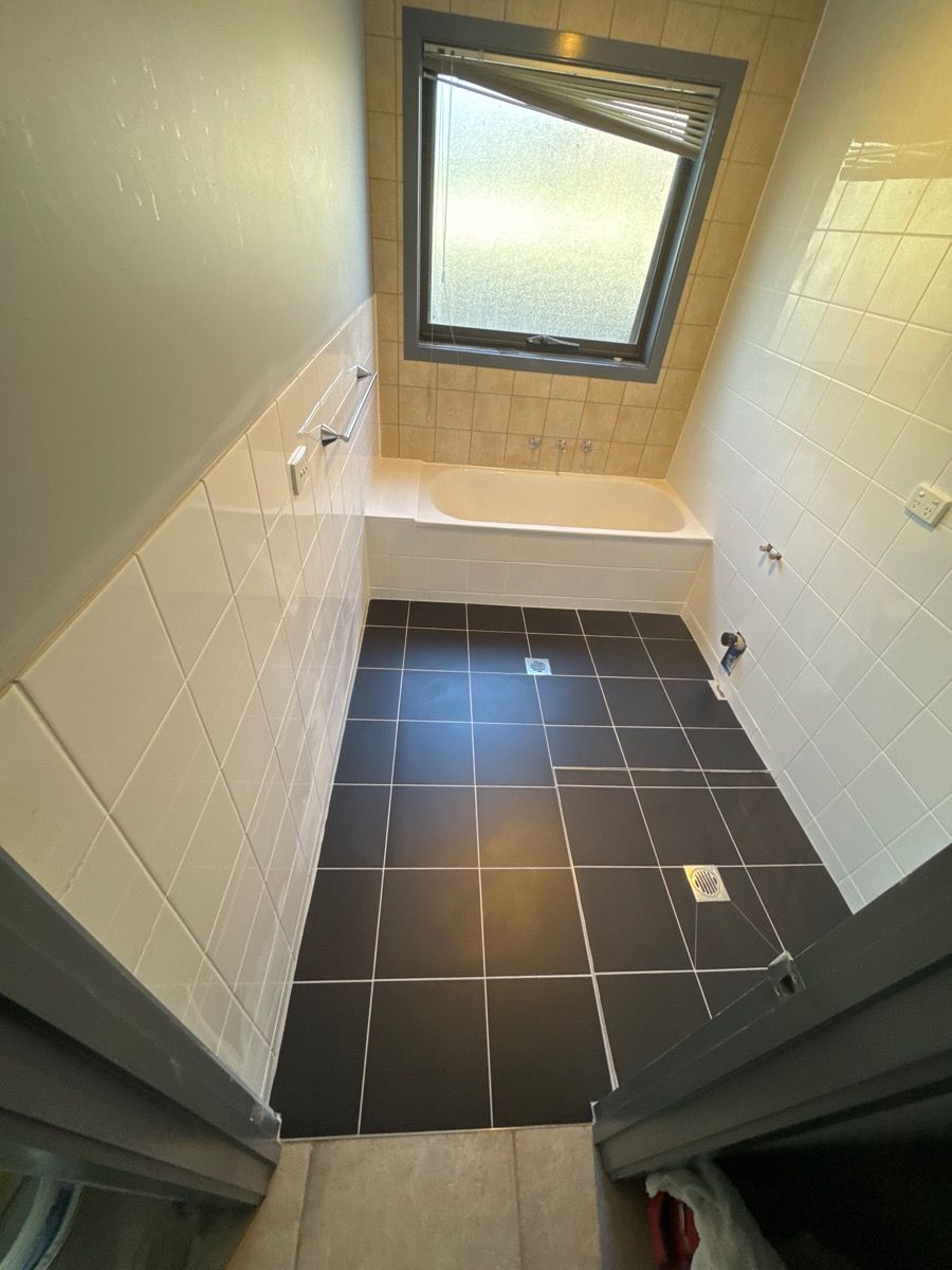 Small bathroom with black tile floor, white walls, tub, and a frosted window. Small bathroom with black tile floor, white walls, tub, and a frosted window.