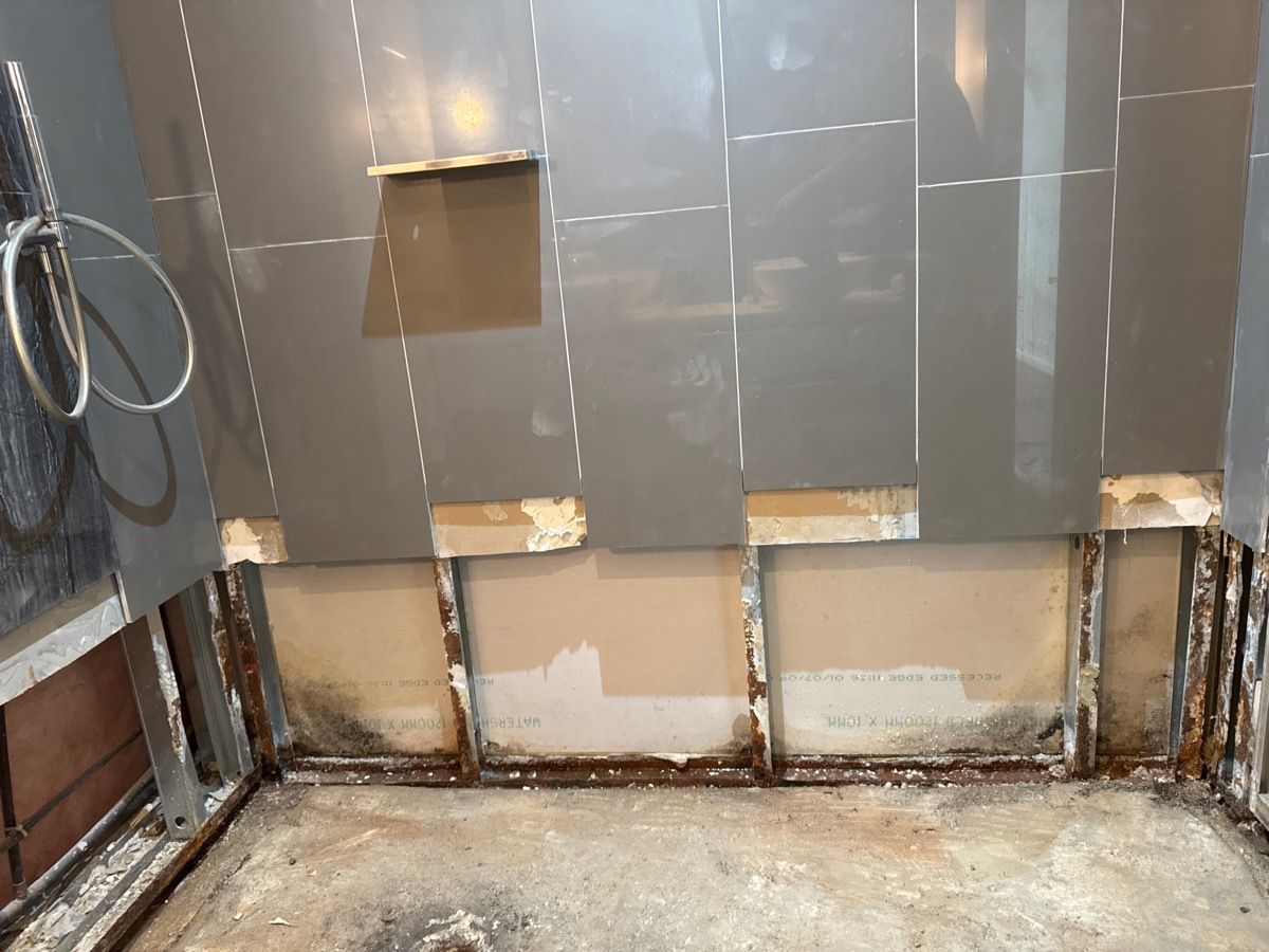 Damaged shower wall with missing tiles and exposed drywall, showing moldy lower sections and a bare shower floor