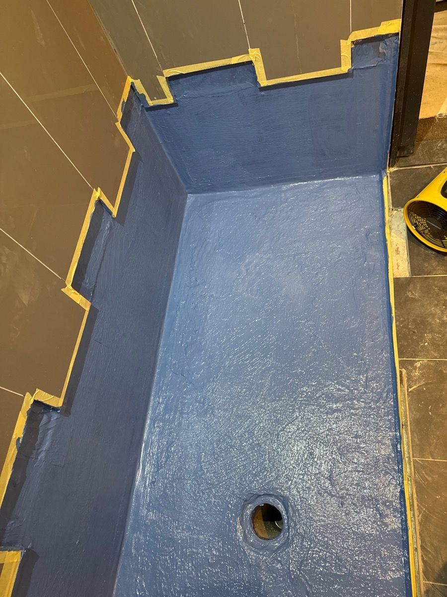 Blue coated floor section with a small drain hole, bordered by tan walls and a yellow hose. Blue coated floor section with a small drain hole, bordered by tan walls and a yellow hose.