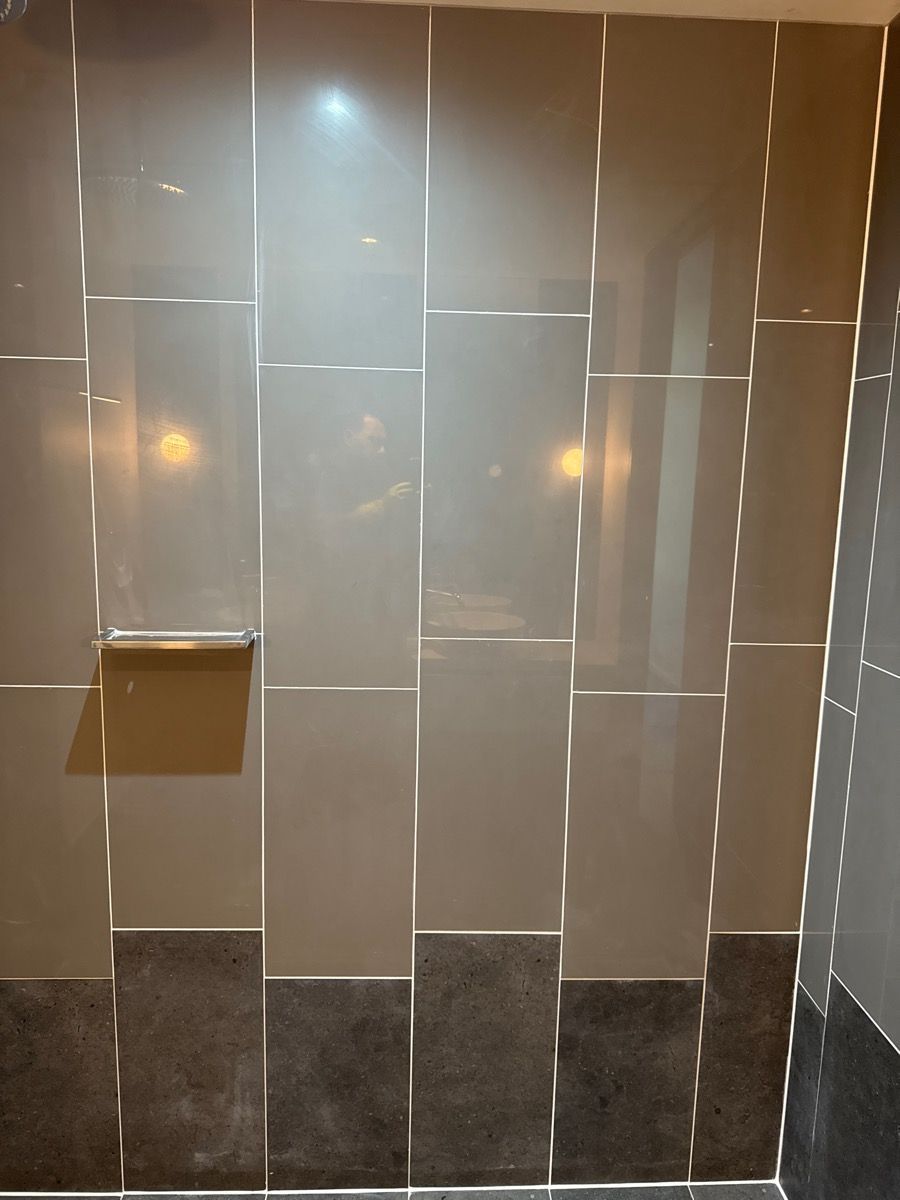 Glossy beige tiled bathroom wall with a small shelf and dark stone base tiles Glossy beige tiled bathroom wall with a small shelf and dark stone base tiles