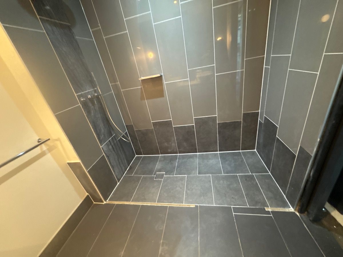 Tiled shower stall with gray walls, dark floor tiles, and a bench-like ledge Tiled shower stall with gray walls, dark floor tiles, and a bench-like ledge