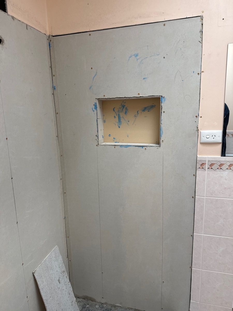 A small tiled bathroom shower stall with a gray unfinished wall and a recessed niche opening.