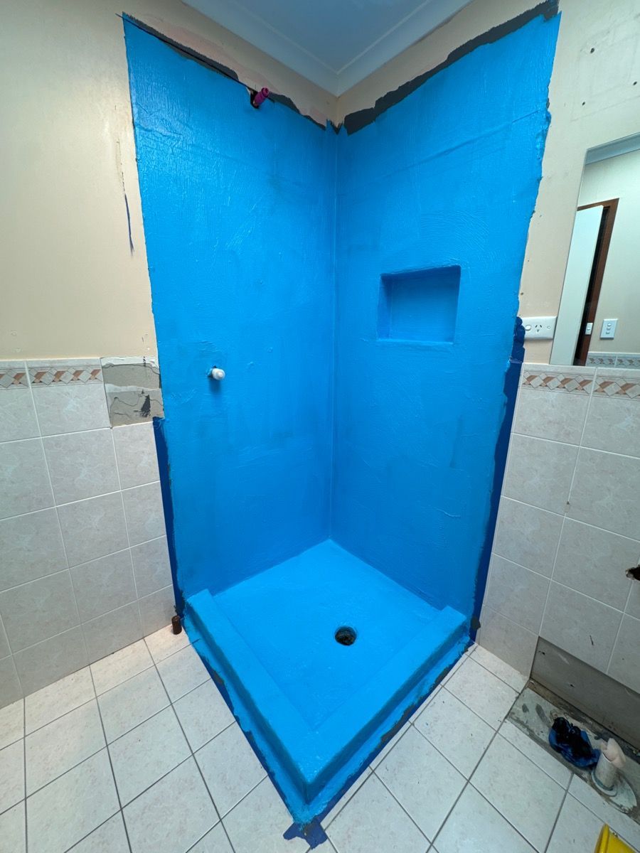 Blue-tiled shower stall with a built-in shelf and floor drain in a tiled bathroom.
