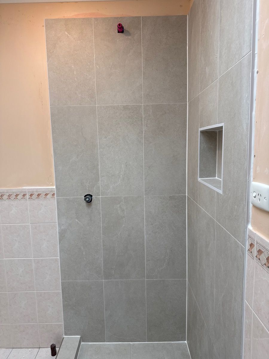 Tiled shower stall with gray walls, built-in niche, and a shower head under construction