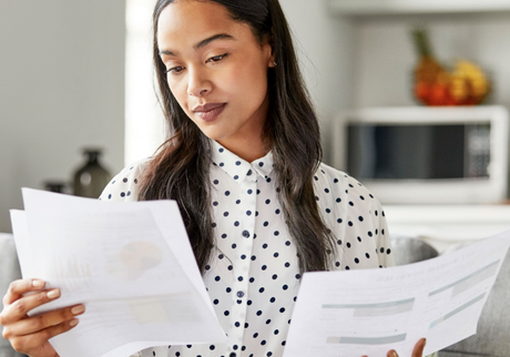 Woman reviewing paperwork indoors; she's focused and dressed in a polka-dot blouse, sitting near a microwave.
