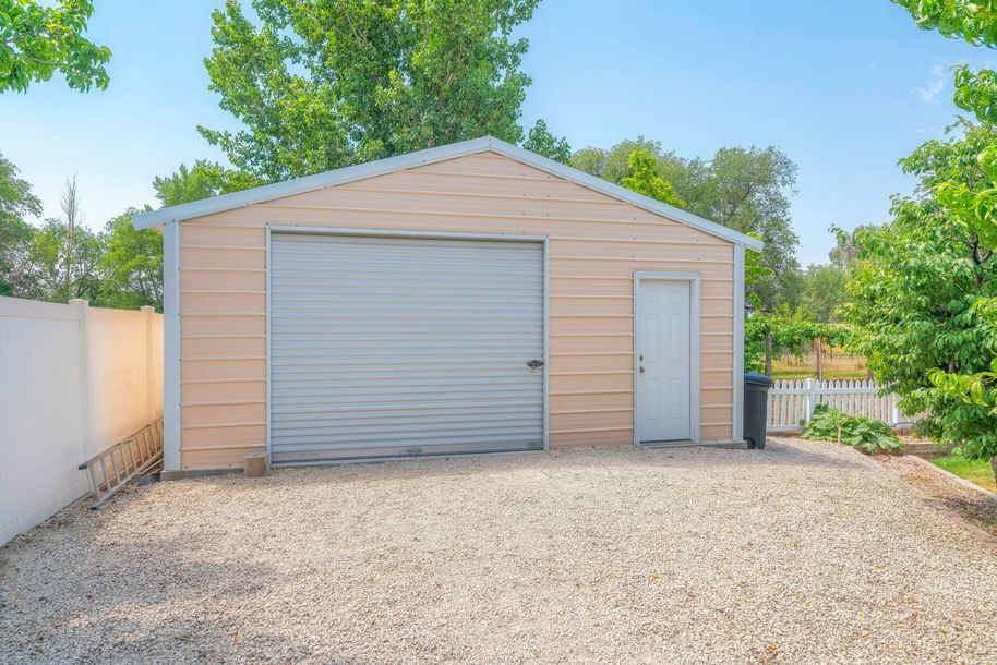 A garage with a gray door and a white door is sitting on top of a gravel driveway