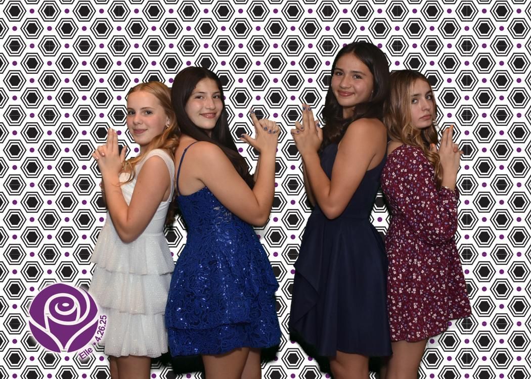 Four young women in formal dresses pose with hands in gun shape against a geometric black and white backdrop.