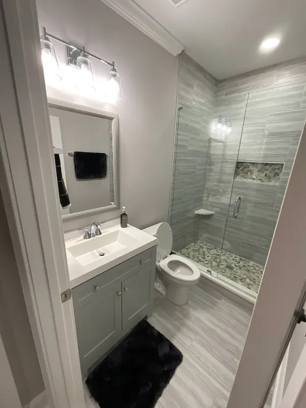 A bathroom with a toilet , sink , mirror and walk in shower.