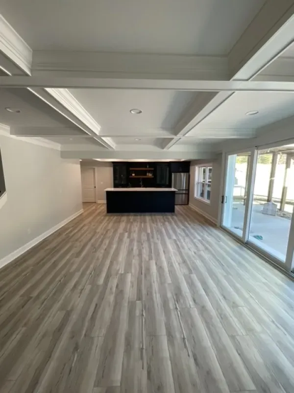 A large empty room with hardwood floors and a kitchen in the background.