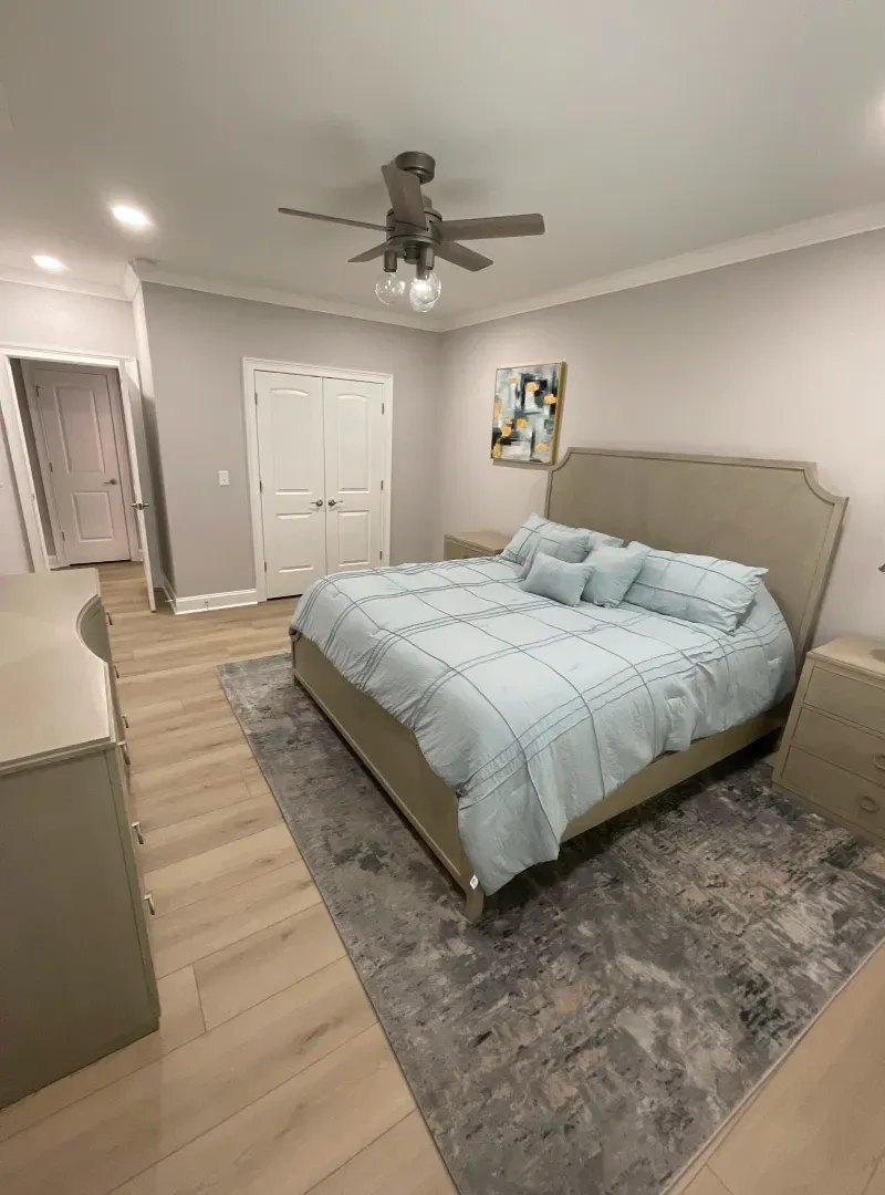 A bedroom with a bed , nightstand , dresser and ceiling fan.