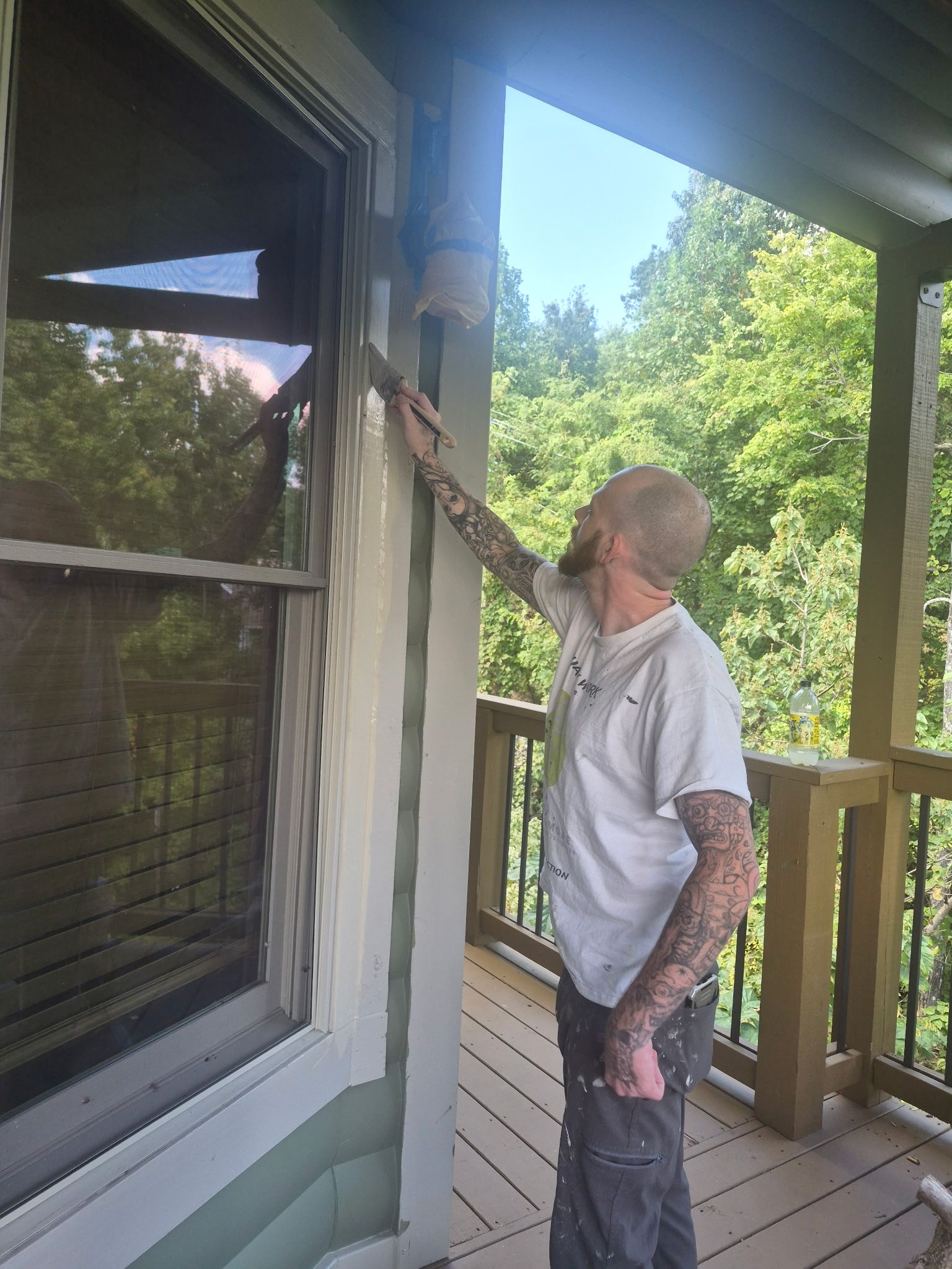 Man reaching up to inspect a house window and trim on a porch in daylight