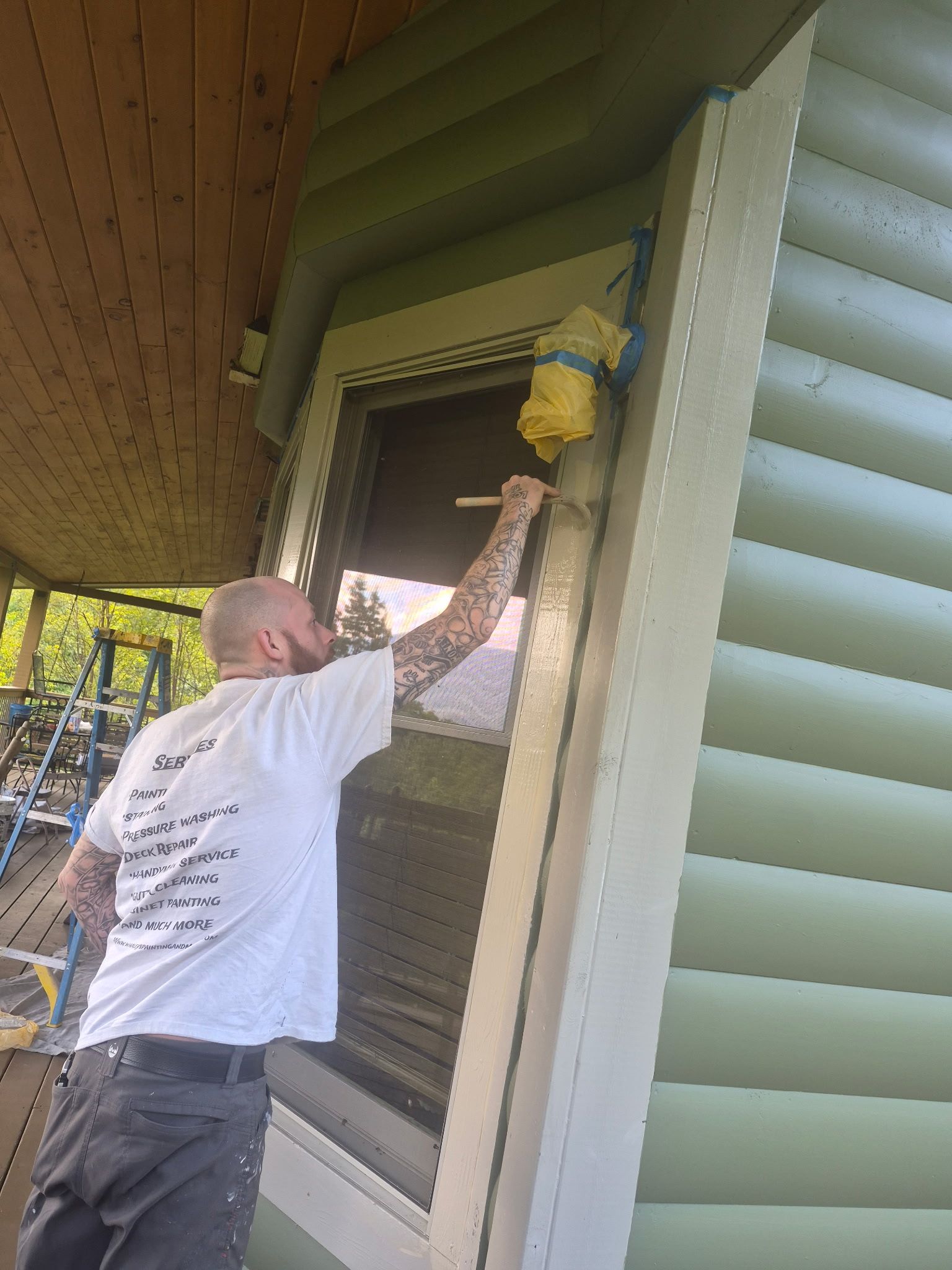 Person painting a house window trim with a roller under the eaves