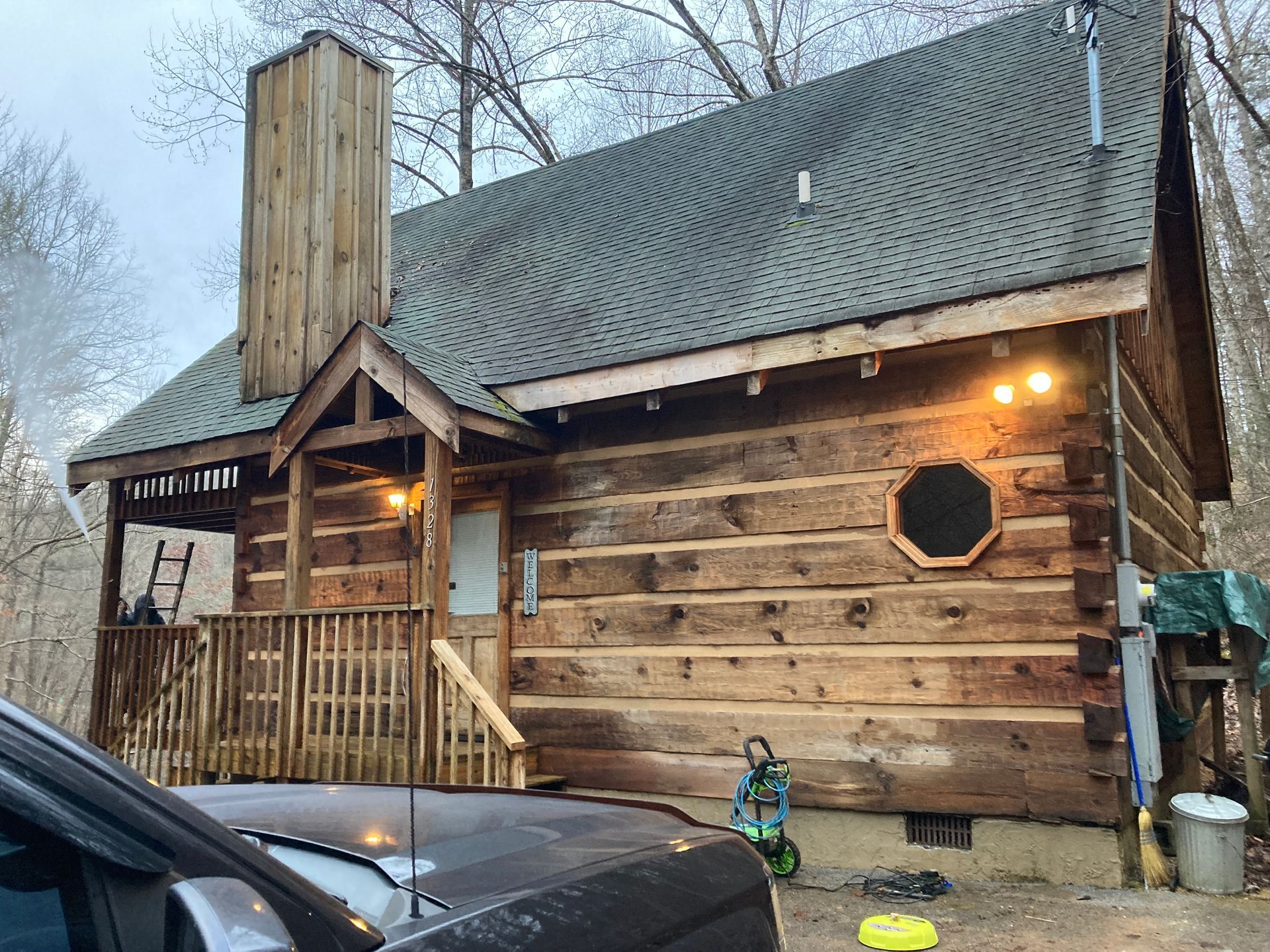 Log cabin with wooden exterior, chimney, porch, and an octagonal window. Child plays nearby.