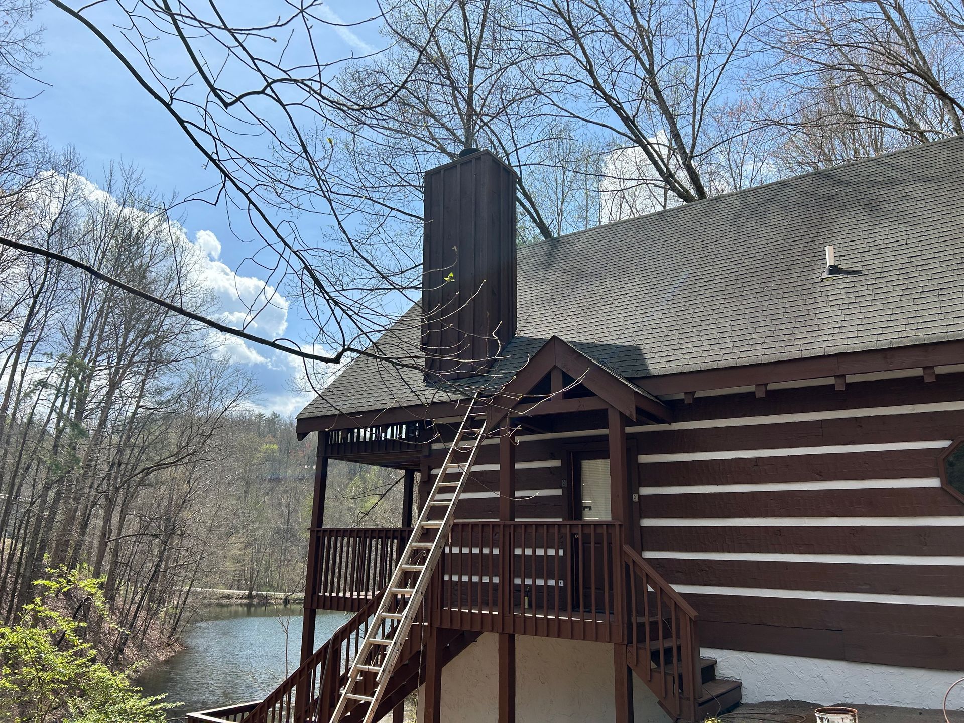 Log cabin with ladder to chimney against a lake, brown with a blue sky.