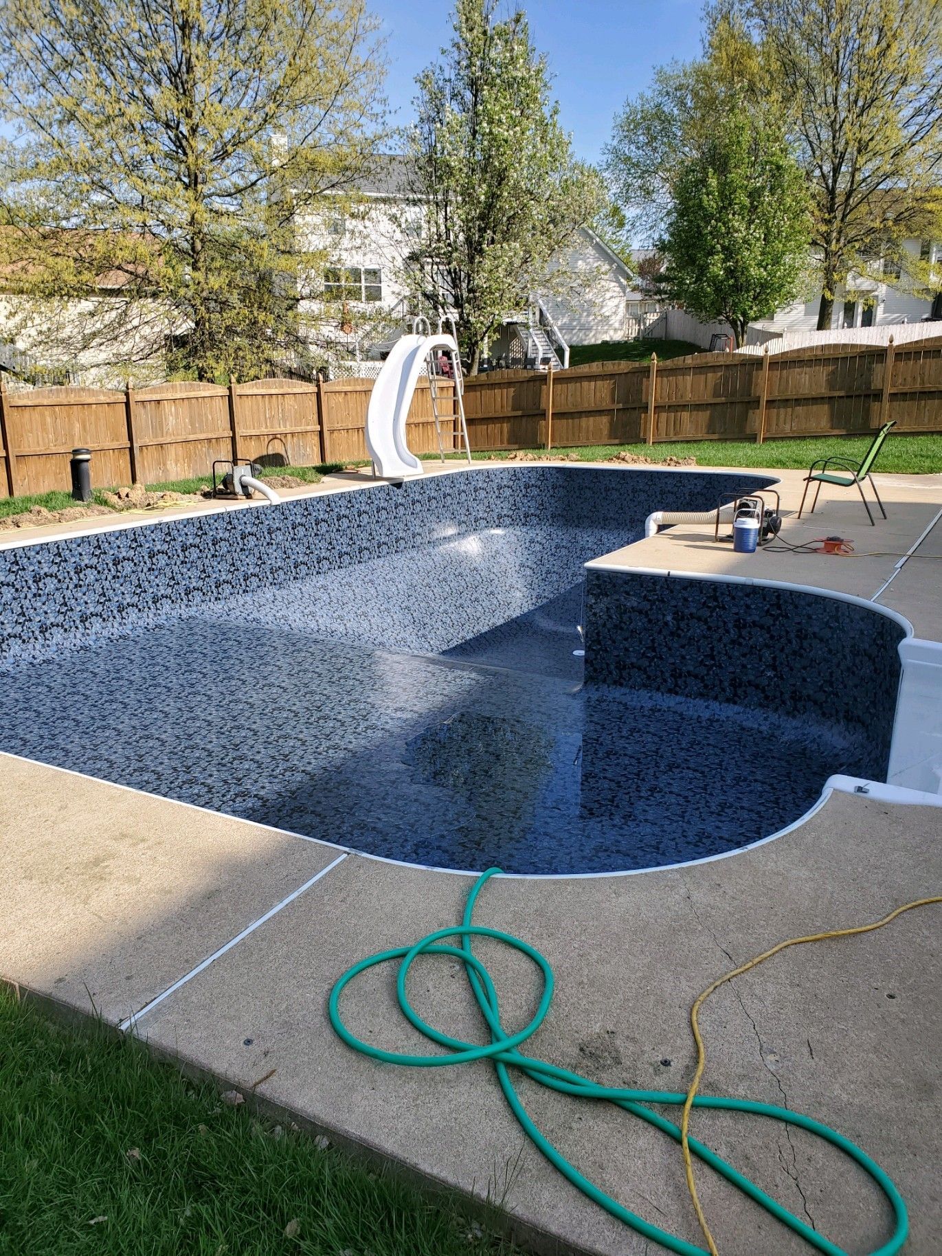 A swimming pool is being built in a backyard with a green hose attached to it.