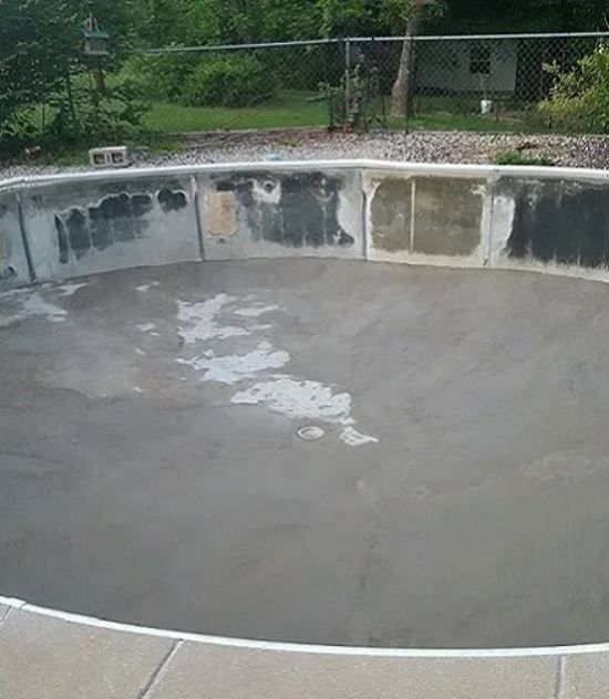 An empty swimming pool with a fence in the background.