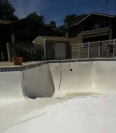 An empty swimming pool with a house in the background.