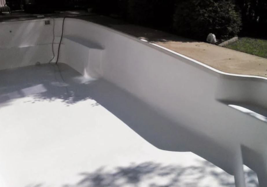 A white swimming pool with a shadow of a tree on the floor