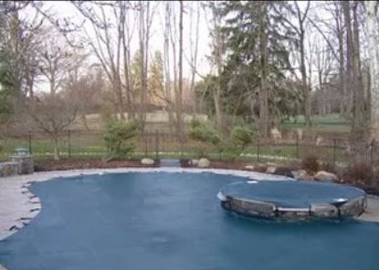 A swimming pool with a blue cover on it is surrounded by trees.