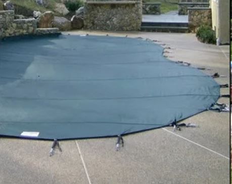 A large green pool cover is sitting on top of a concrete driveway.