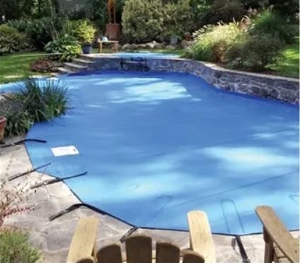 A swimming pool with a blue cover and two chairs in front of it.